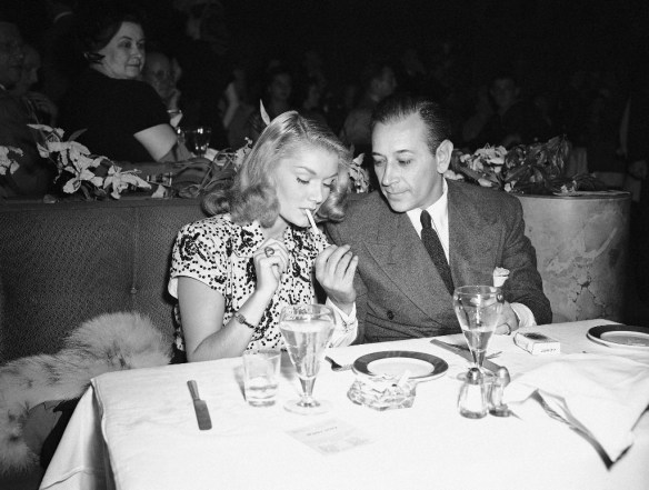 Screen star George Raft lights a cigarette for his date, actress Eve Amber, during an evening at Ciro’s in Hollywood, Los Angeles on August 17, 1945. (Associated Press photo)