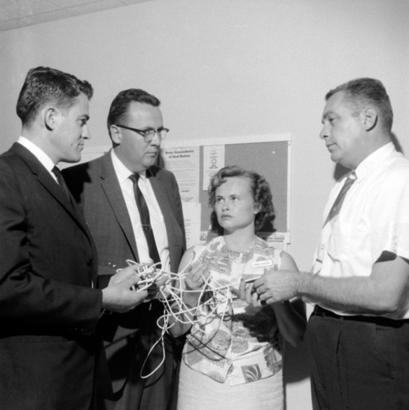 L to R: Pacific State Bank manager Keith Pischel, assistant manager Emerson Kreiger and teller Bonni Farquhar show clothesline used by robbers to tie up employees to unidentified police investigator in this Oct. 5, 1963 Daily Breeze file photo.