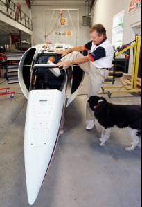 Craig Breedlove, 60, climbs out of the cockpit of his $3 million rocket-powered car as his border collie Muffin watches in the garage and headquarters of Spirit of America in Rio Vista, Calif., Wednesday Aug. 27, 1997. Photo credit: The Associated Press.