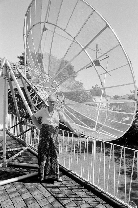 At home in the future, science fiction writer Arthur C. Clarke pauses near his personal satellite antenna at his residence in Colombo, Sri Lanka, Jan. 28, 1977. He uses the device to received programs beamed from India in an experiment to broadcast educational programs through space. The antenna and television, the only one in Sri Lanka, were gifts of the Indian government. (AP Photo/Denis Gray)